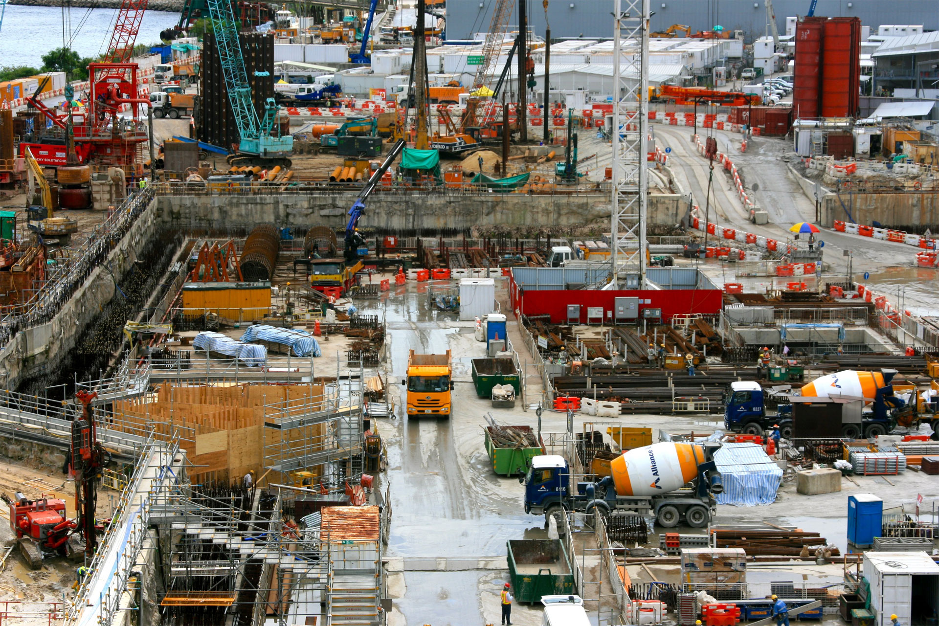 View from above of a large construction site with cranes, ready-mixed trucks, other lorries and construction workers