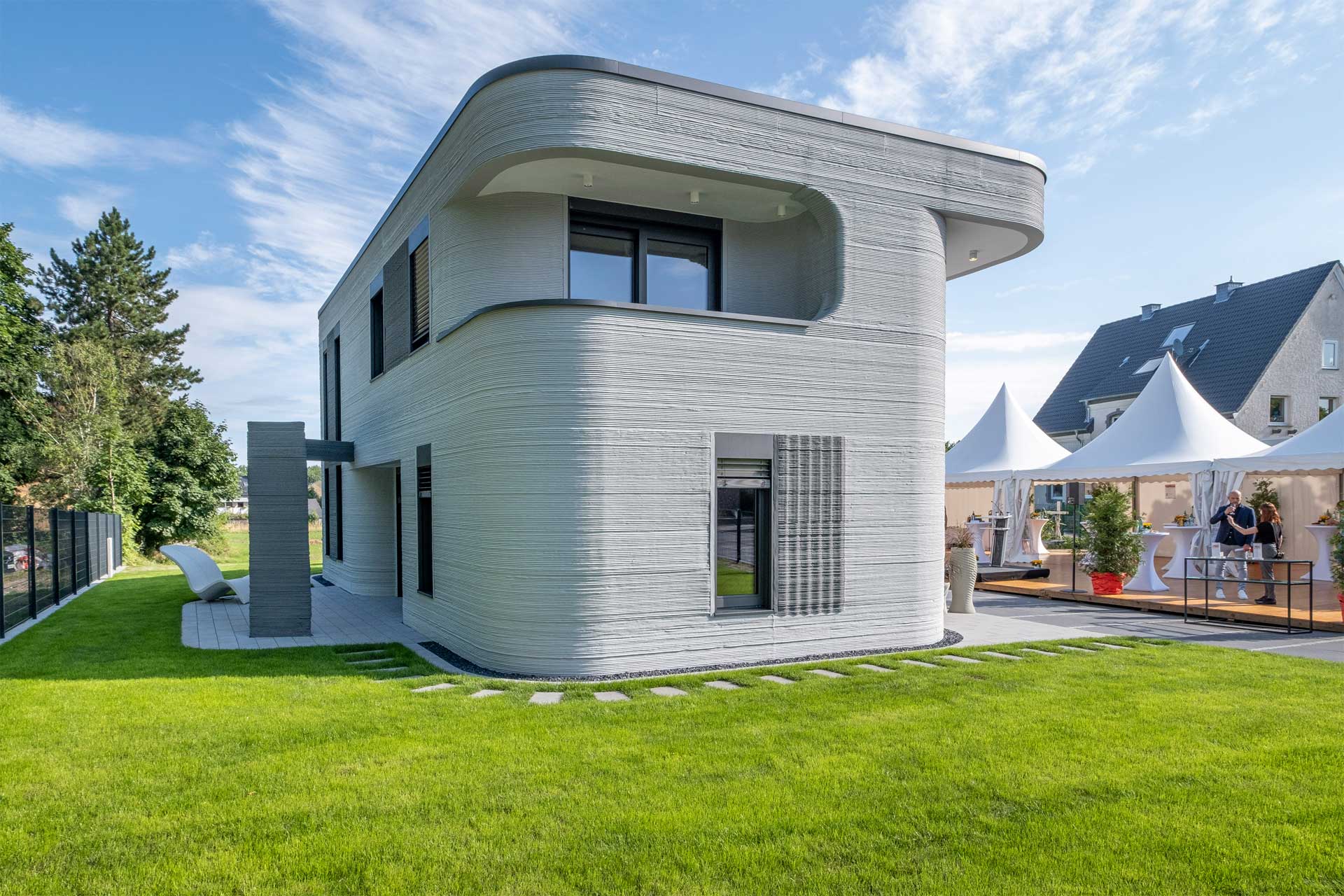 Modernes zweistöckiges Haus mit geschwungenem Design und strukturierter Außenfassade, auf gepflegtem Rasen unter blauem Himmel