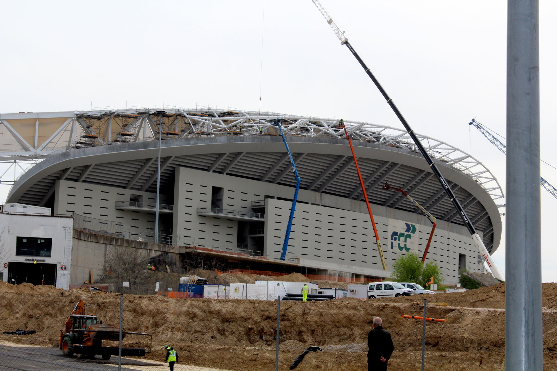 Weitläufige Baustelle eines großen Stadions, das die komplexe Struktur von Kränen und Gerüsten unter einem klaren Himmel präsentiert