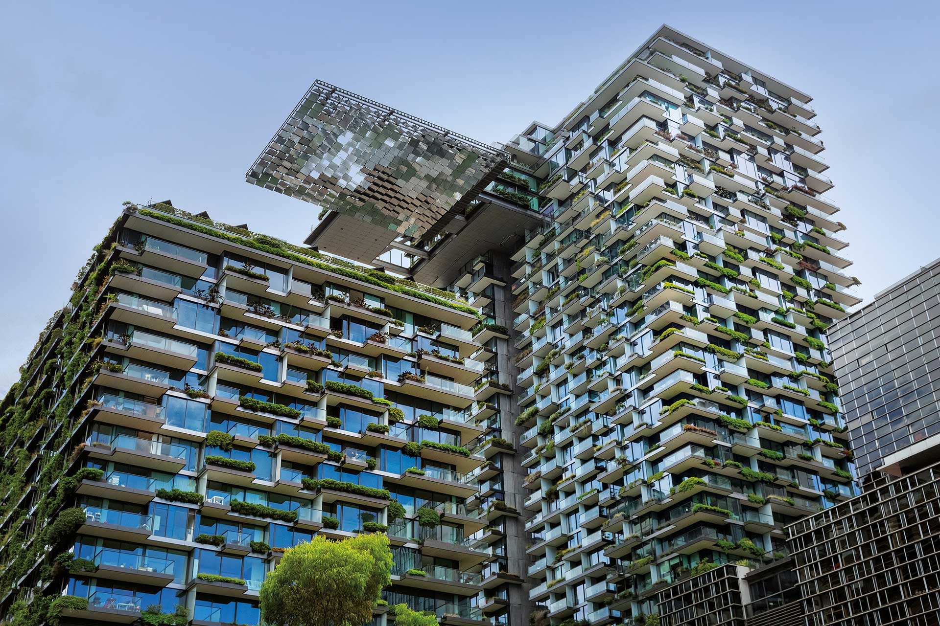 A contemporary multi-story building featuring lush greenery on every balcony, showcasing eco-friendly architectural design
