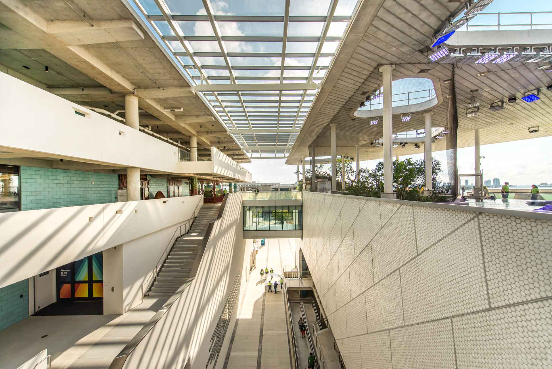 A contemporary interior showcases a multi-tiered layout with a translucent ceiling, bathing the space in daylight. The walls are lined with uniform square tiles, and the upper level features prominent circular windows.