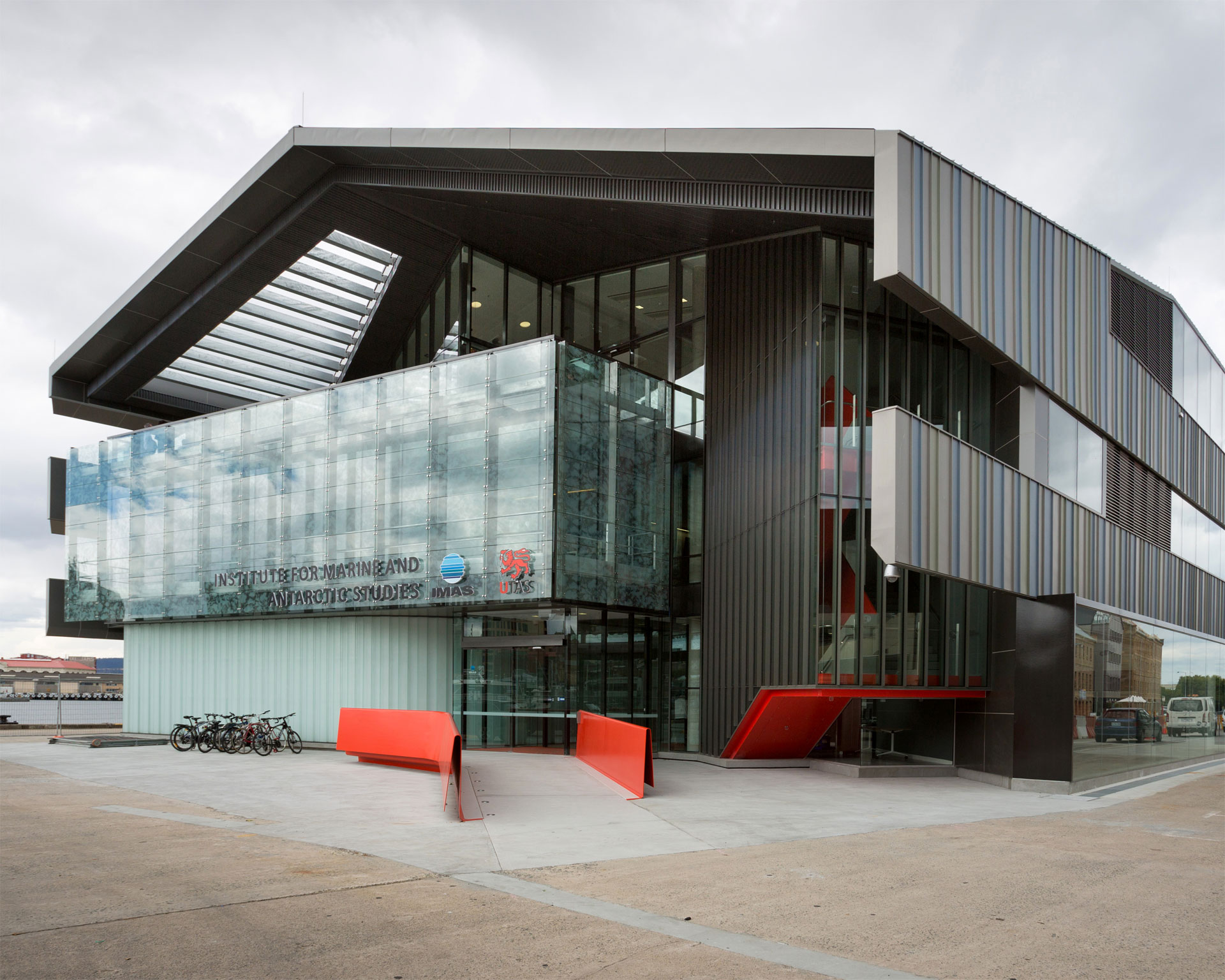 A modern building with glass and metal features, red benches in front, and a row of parked bicycles