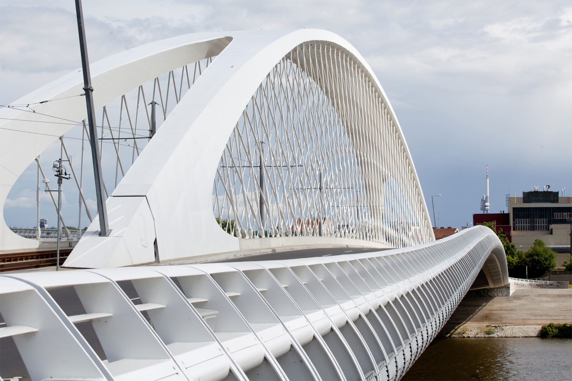 A modern white bridge with a curved design over a river, under a cloudy sky