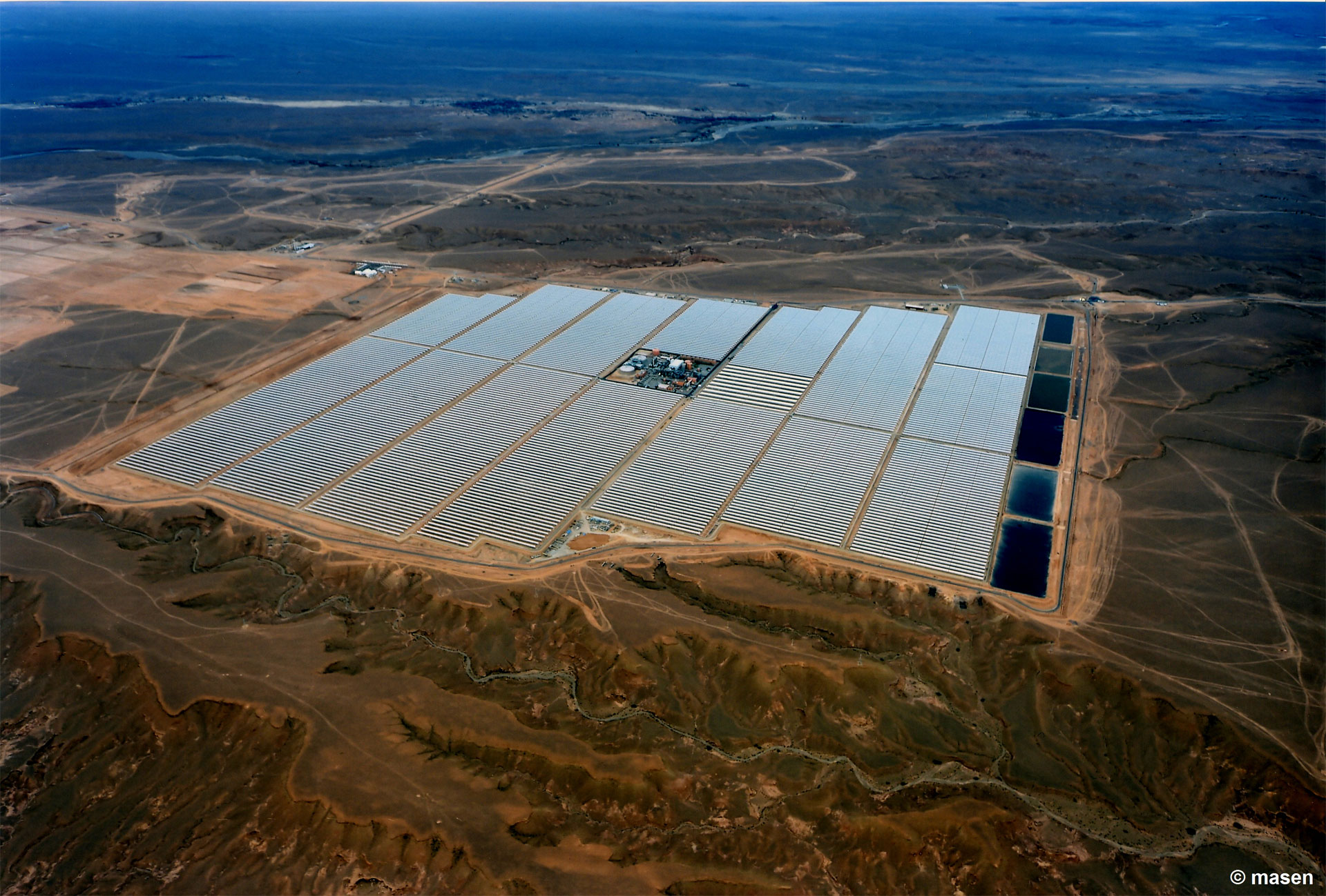 Aerial view of a large solar farm with rows of photovoltaic panels, surrounded by arid terrain