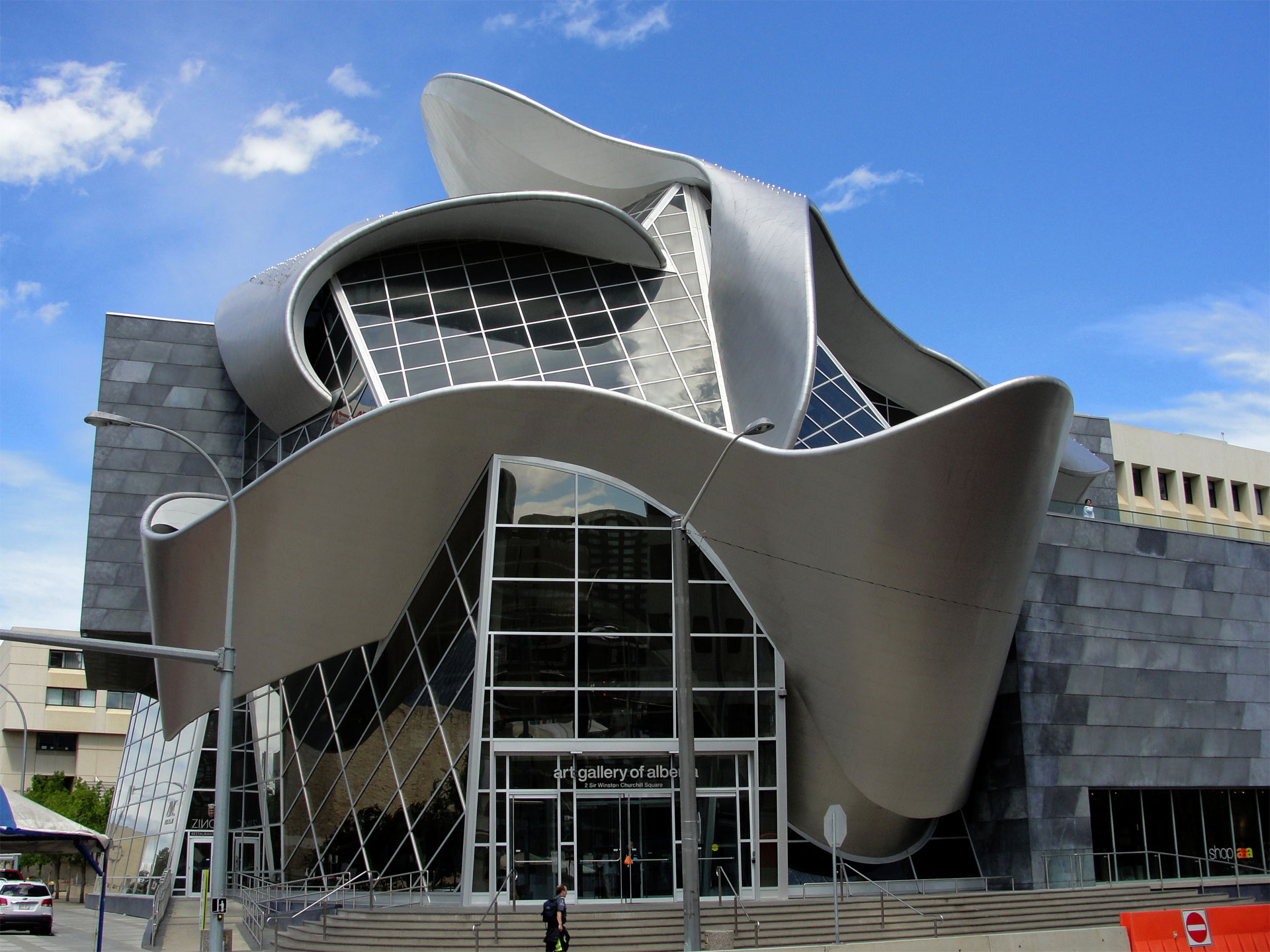 A modern art museum with a distinctive architectural design featuring metallic curves and glass elements under a blue sky with clouds