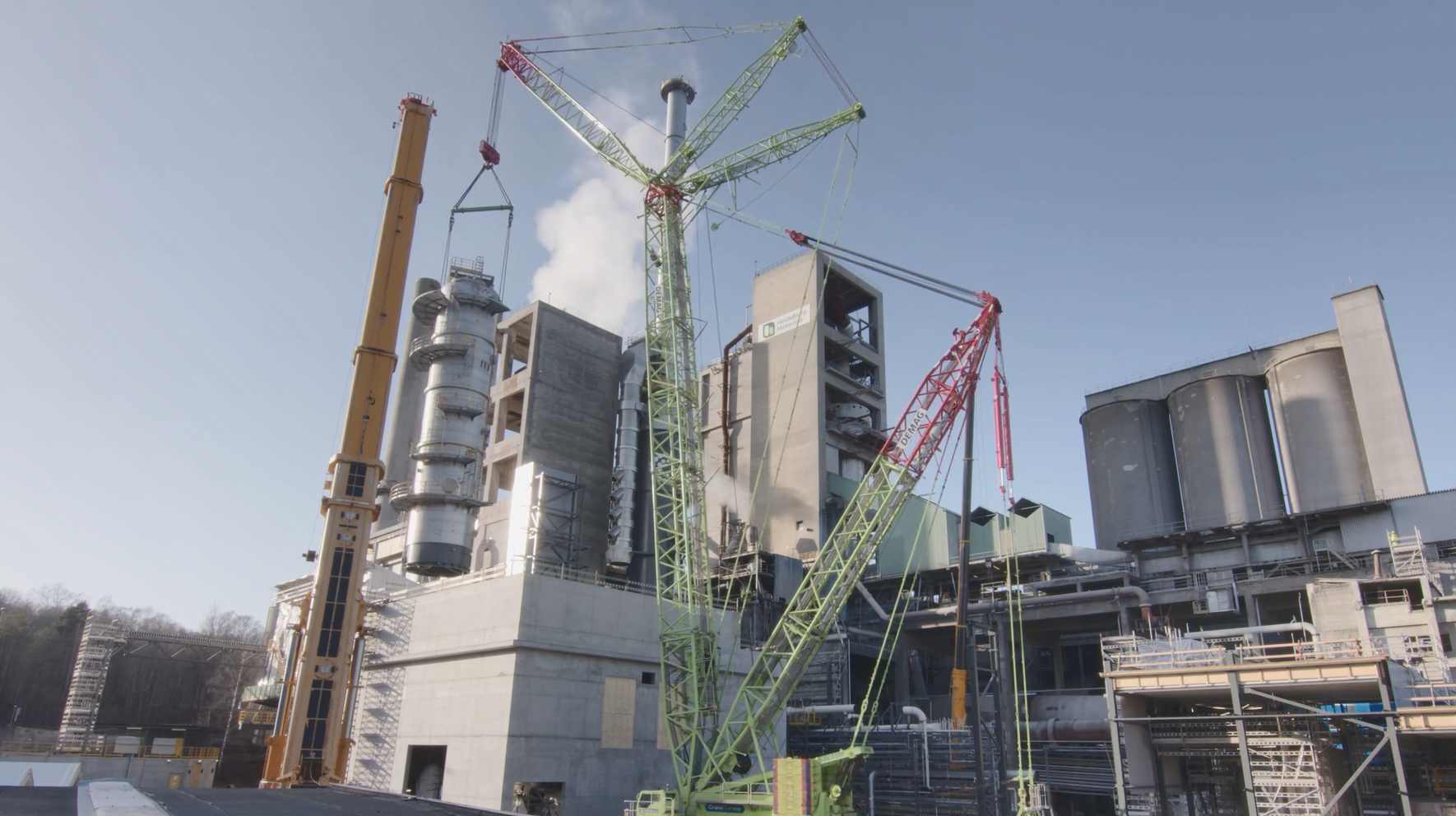 A green crane at a cement plant under a clear sky
