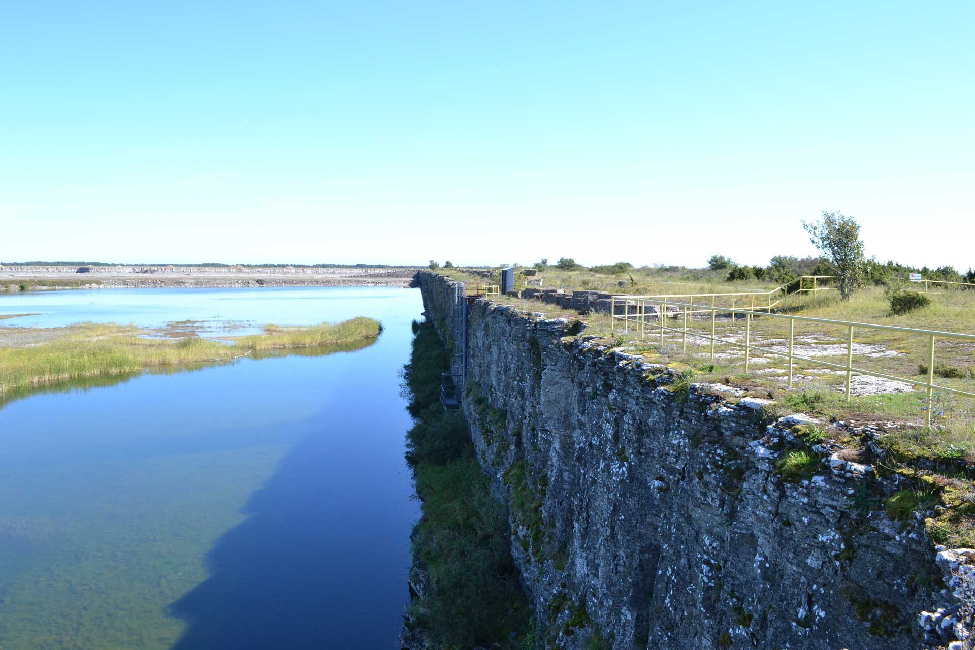 A blue lake inside an abandoned quarry, a mine can be seen in the far distance