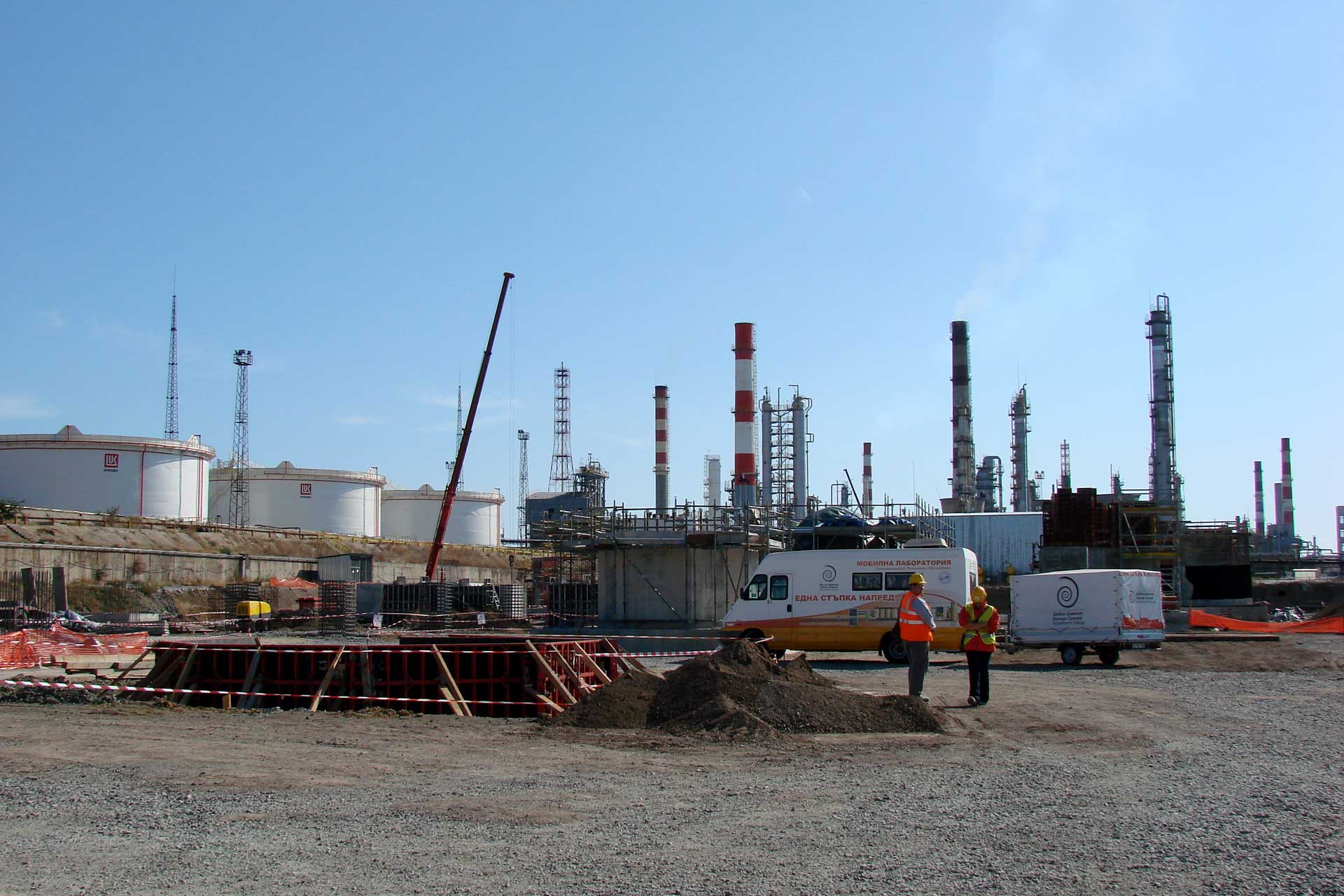 An industrial setting with multiple large cylindrical storage tanks and tall chimneys emitting no visible emissions against a clear sky.