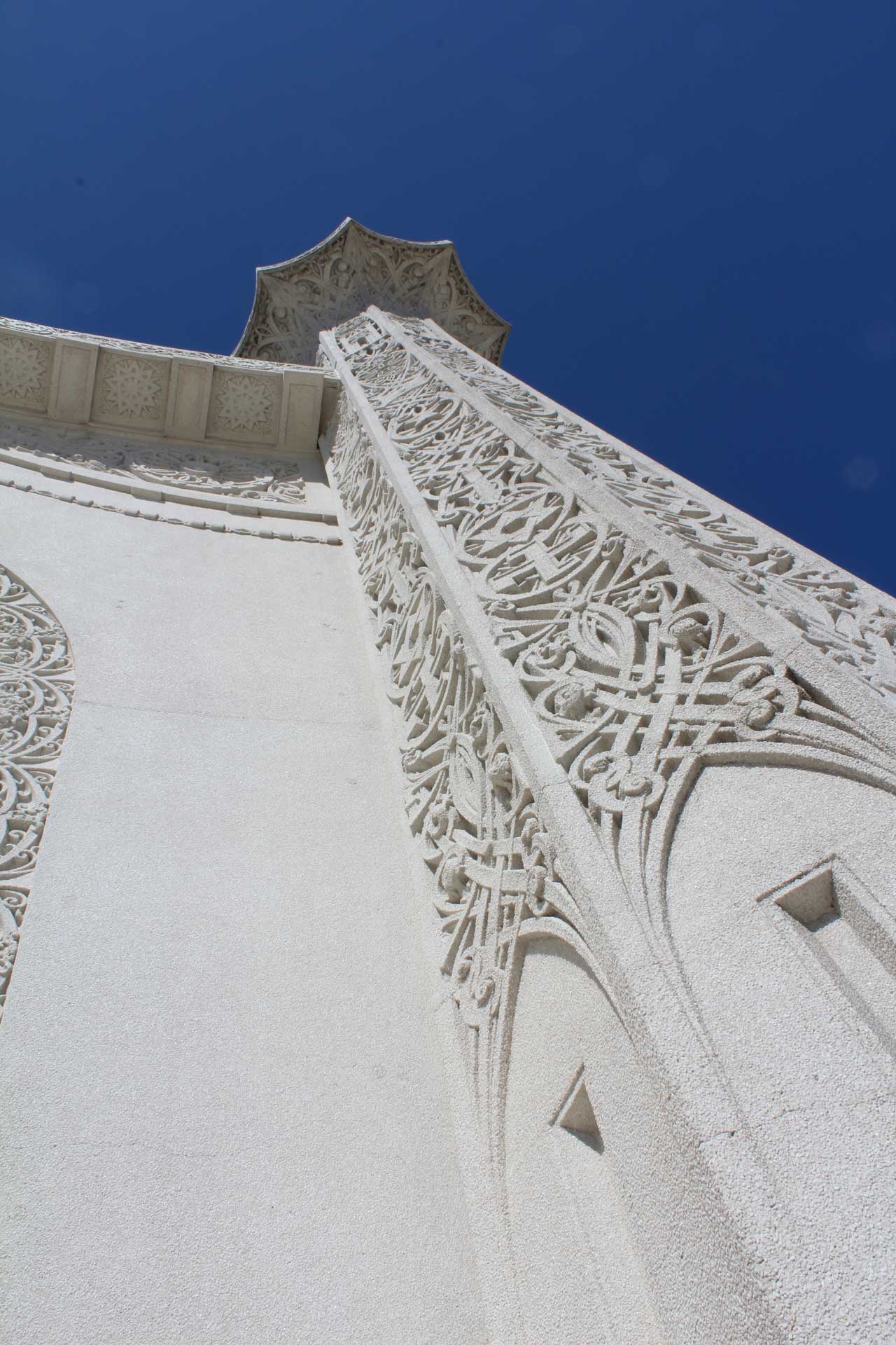 A white building with intricate designs on its facade, leading up to a tower against a clear blue sky. The architectural details suggest its cultural significance.