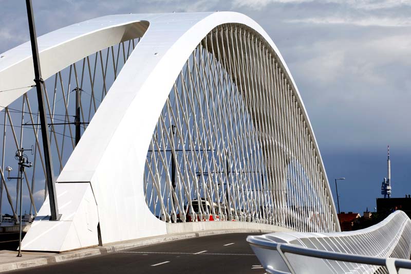 Modern bridge with a distinctive, curved white structure forming an arch over the roadway. The design features a network of triangular patterns created by intersecting metal supports within the arch.