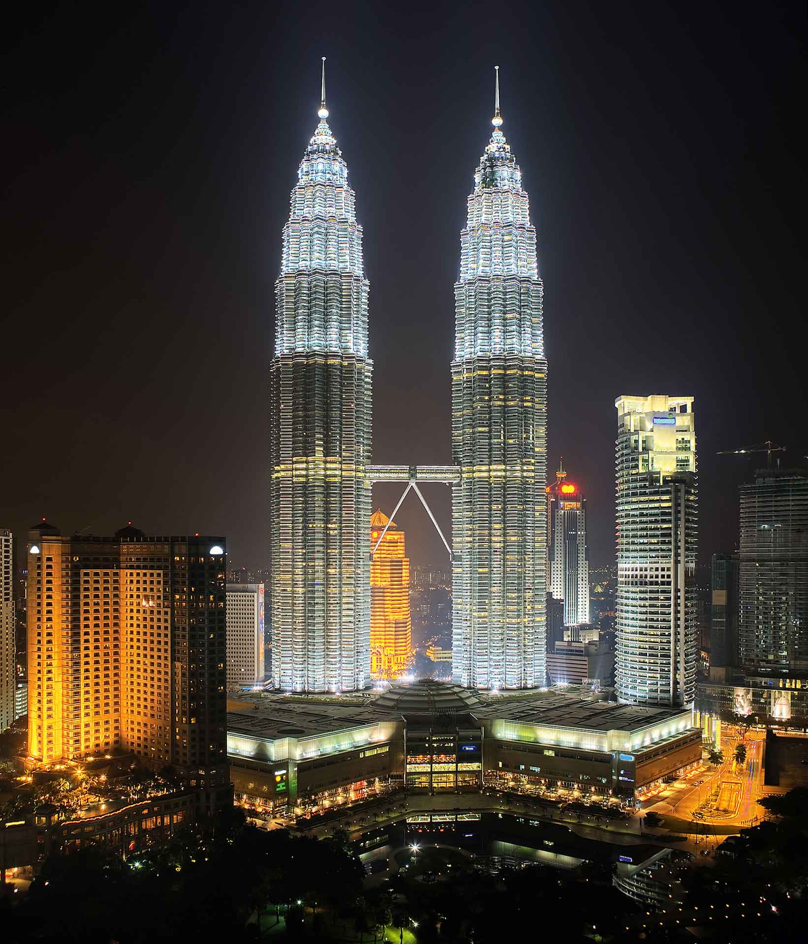 The Petronas Twin Towers at night, illuminated against a dark sky. These towers are notable for their height and architectural design, featuring a postmodern style with Islamic-inspired details.