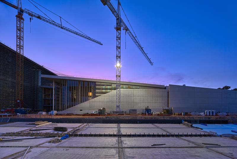 A construction crane stands next to a building under construction during twilight; the foreground features a frozen construction site with tyre tracks.