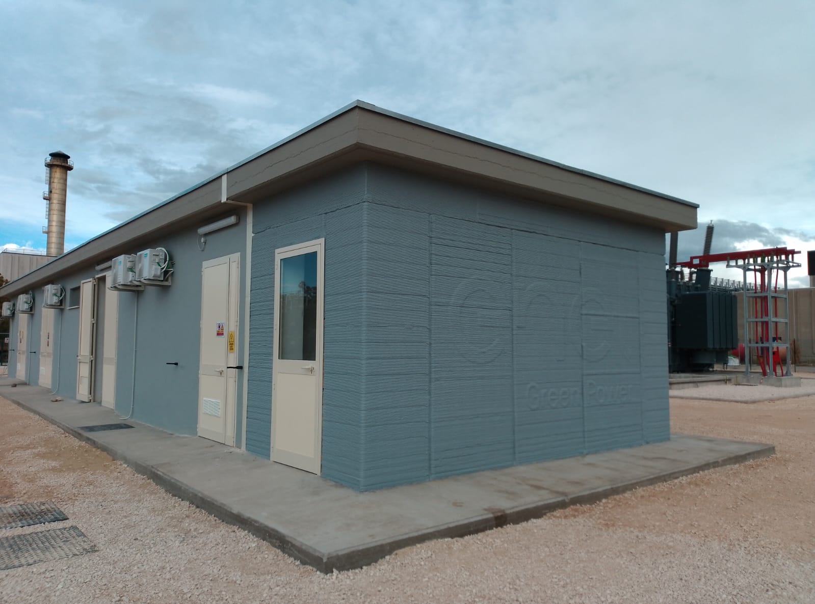 A light grey, single-story building with two doors but no windows under a cloudy sky.