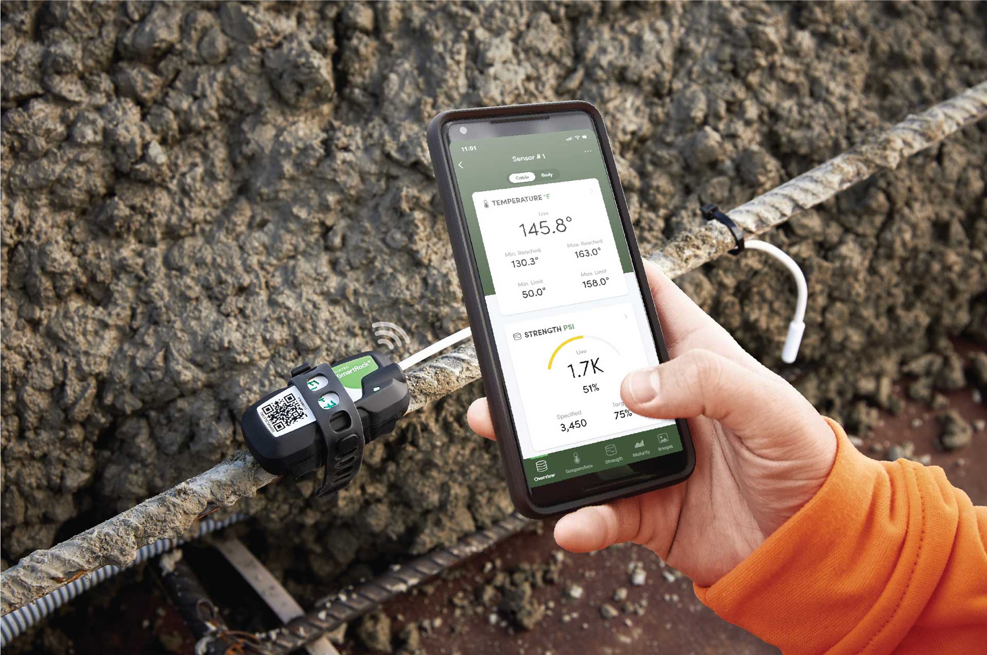 A person using a smartphone to monitor construction data. The phone screen shows temperature and strength measurements. A person using a smartphone to monitor construction data. The phone screen shows temperature and strength measurements, as well as a QR code.