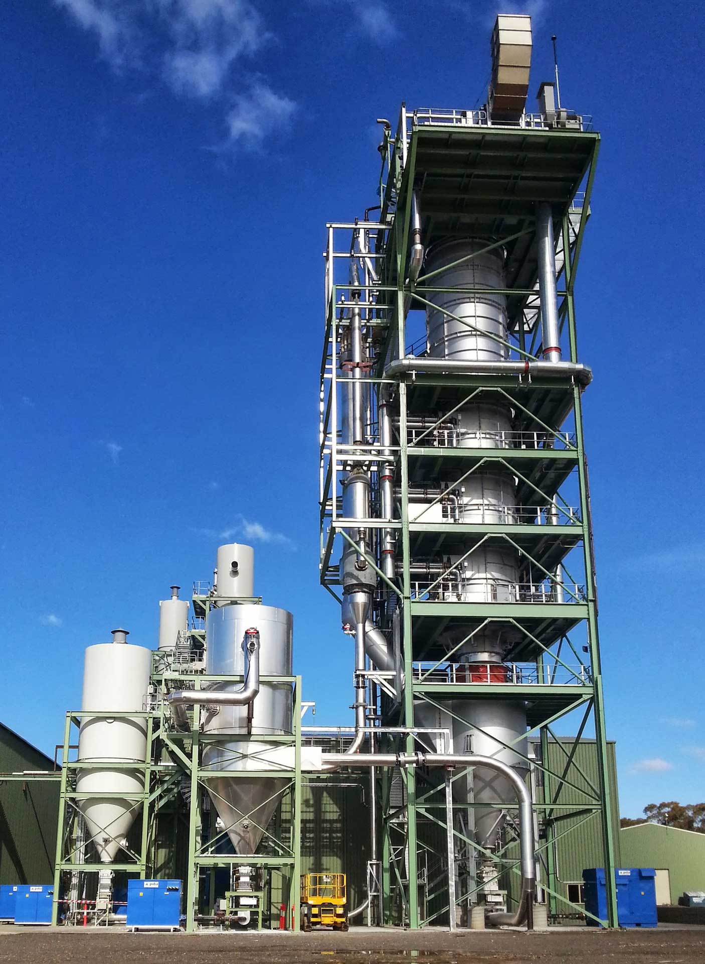 Eine große, industrielle Anlage mit einem hohen, mehrstufigen Teilen im Zentrum. Mehrere kleinere Tanks und Rohre sind mit der Säule verbunden.