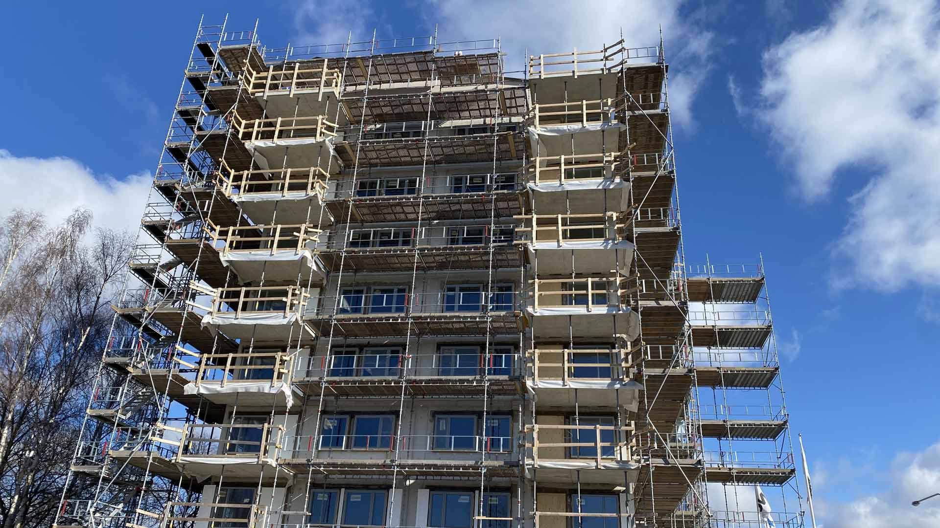 A multi-storey building with scaffolding in front of a blue sky with a few clouds.