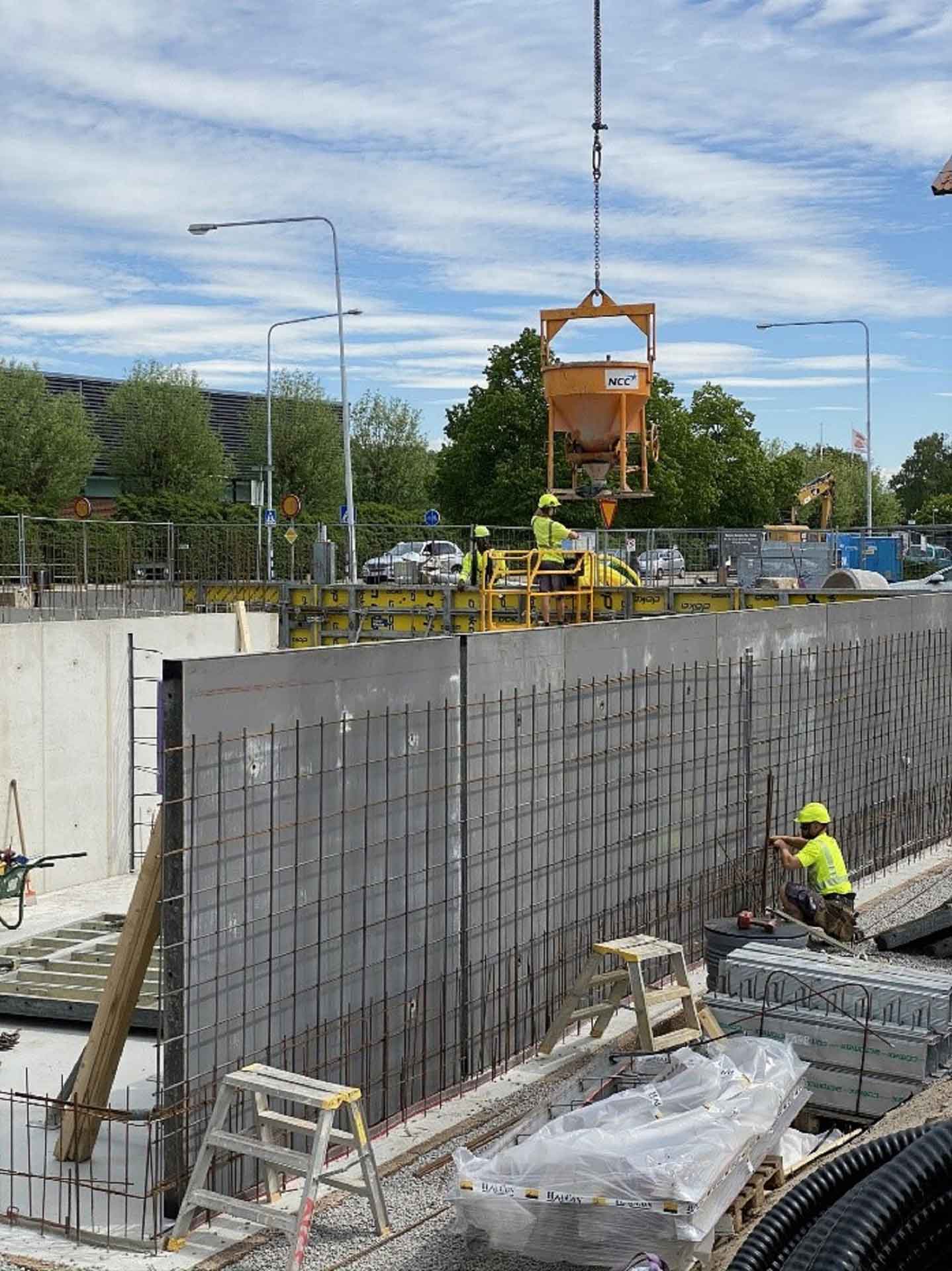 An excavation pit with concrete walls and steel mesh, above which a container hangs from a crane.