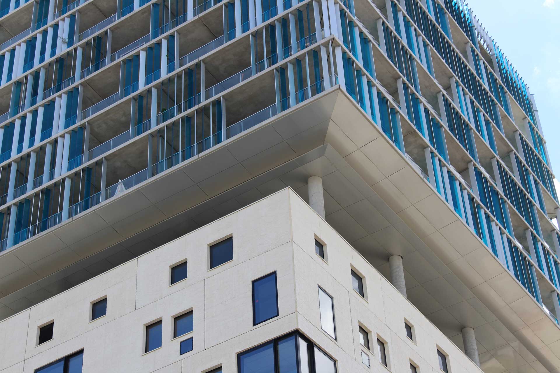 A modern multi-story building with white lower floors and upper floors featuring glass balconies and blue accents.