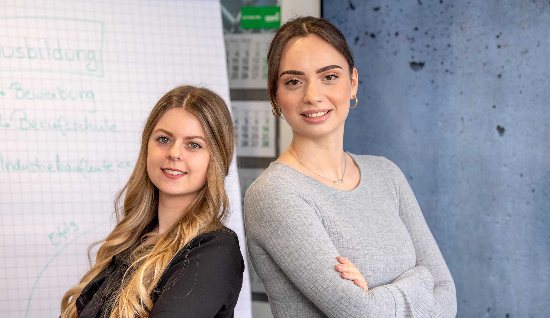 Zwei junge Frauen stehen Rücken an Rücken vor einem Flipchart