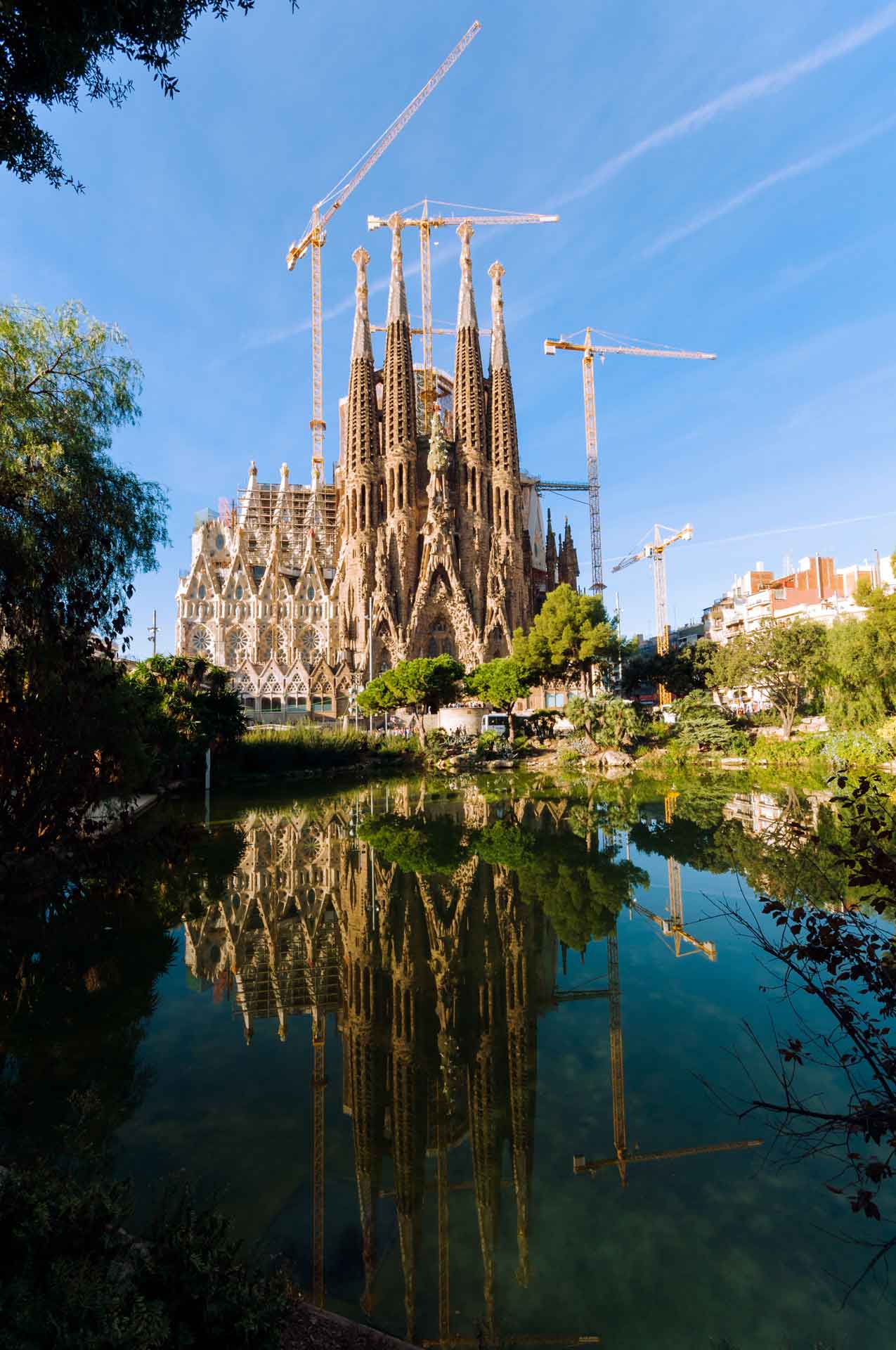 The Sagrada Familia basilica in Barcelona, Spain, with its iconic spires and intricate facade under construction, mirrored in the water below.