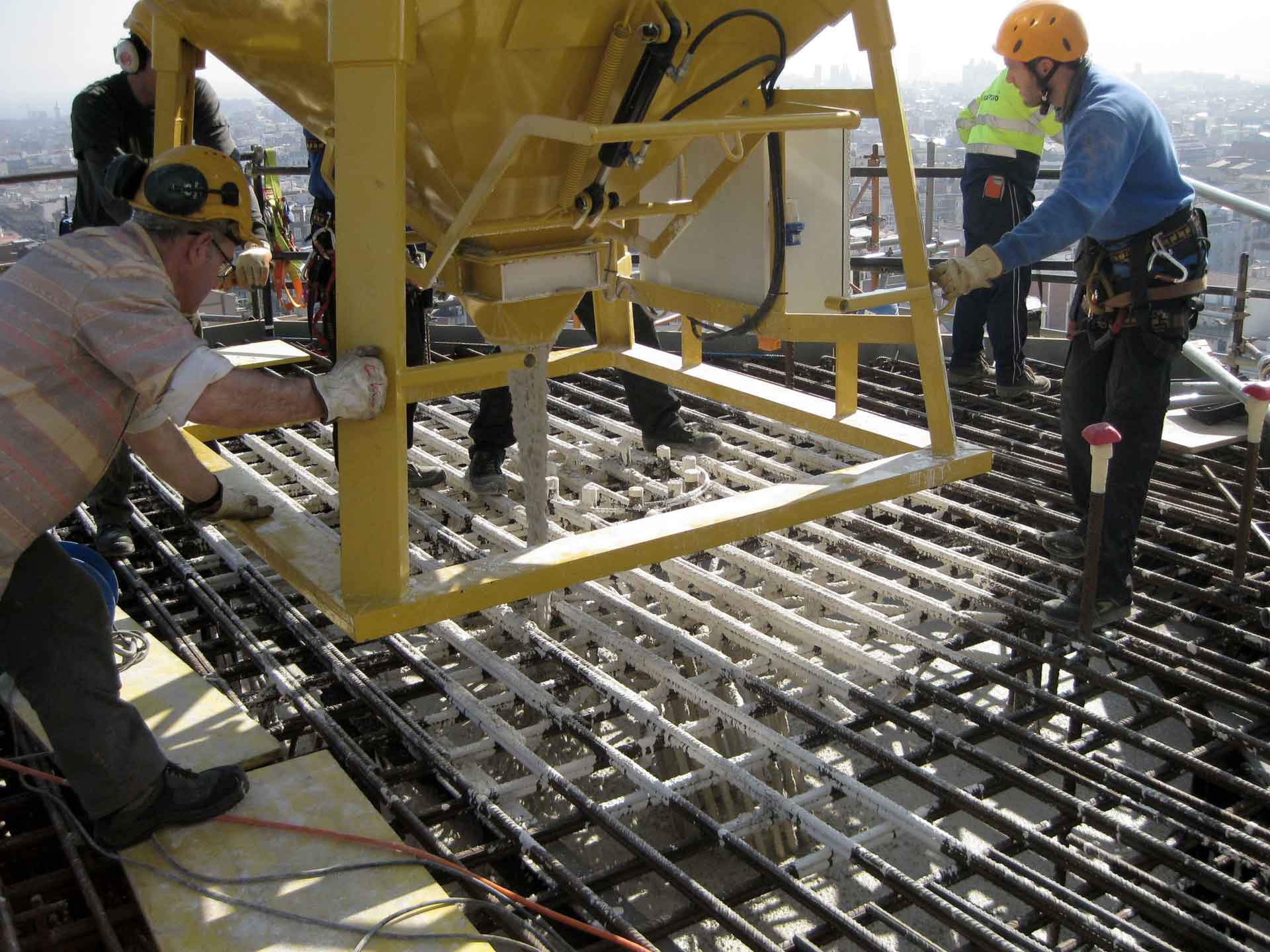 In the image, two construction workers are seen working on a building site. One is operating machinery to pour concrete, while the other oversees the process.