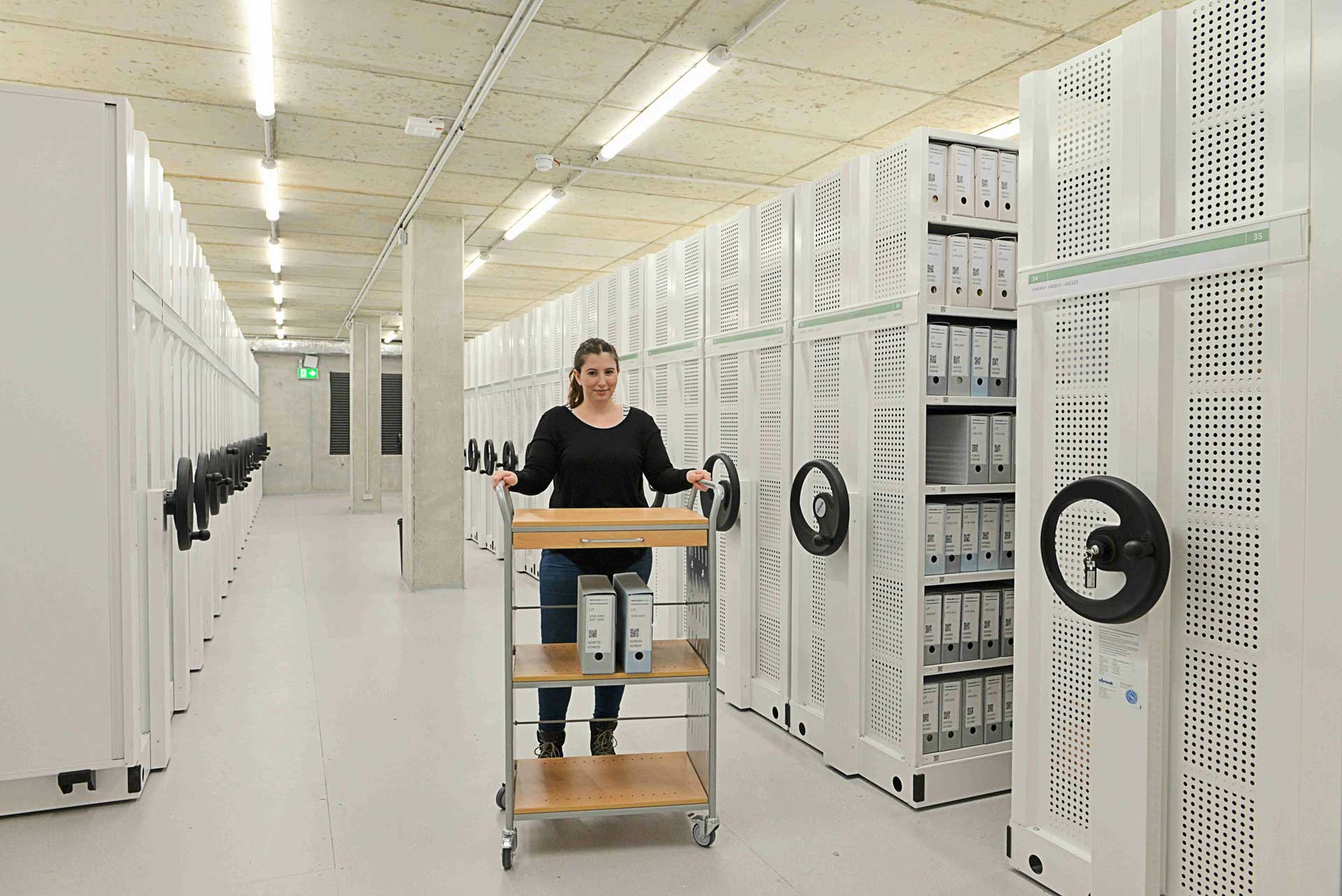 Woman transporting files on a trolley between filing cabinets