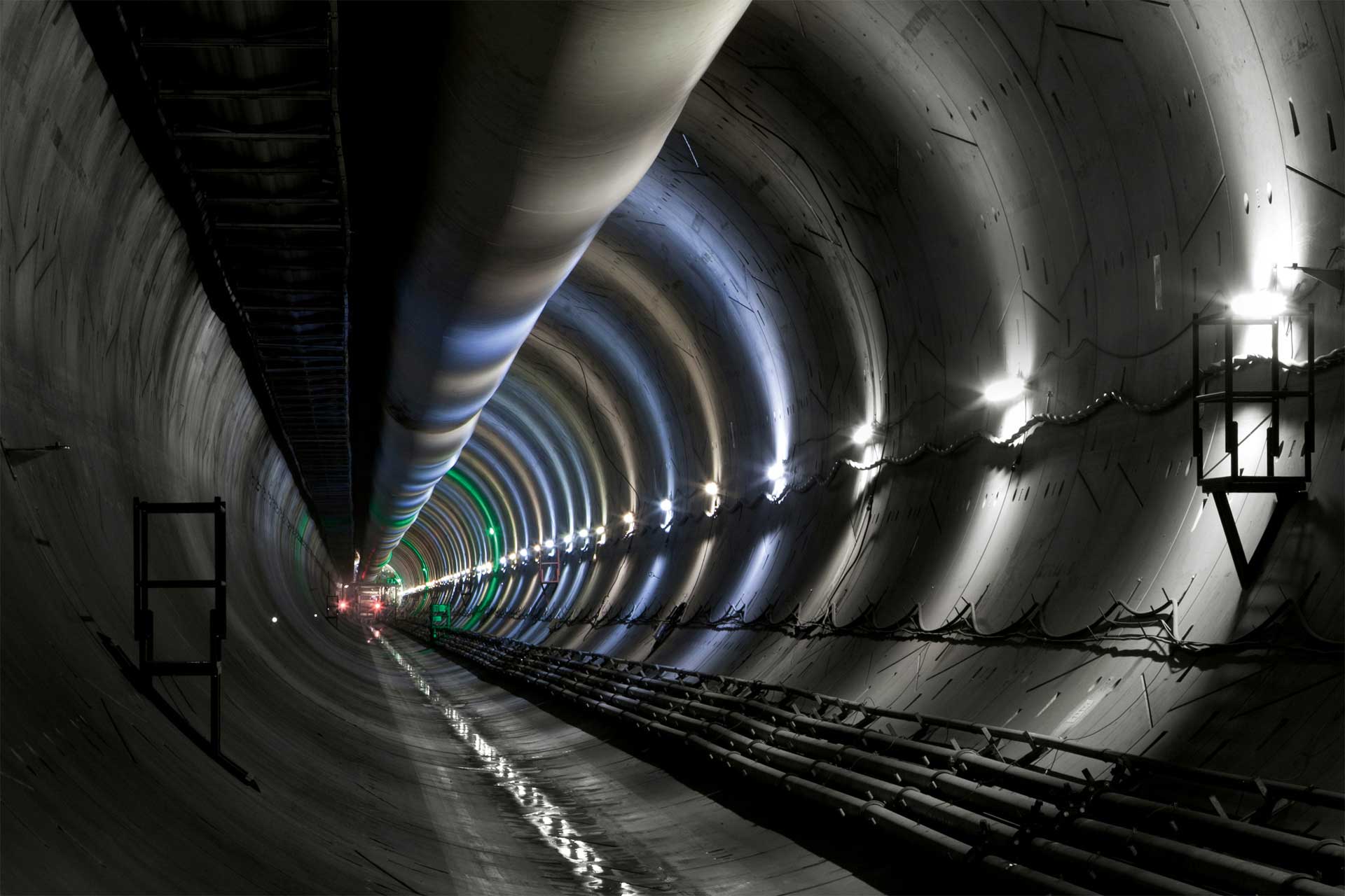 Innenansicht eines langen, beleuchteten Tunnels mit reflektierenden Wänden und Decke, zeigt Lichter und Konstruktionselemente