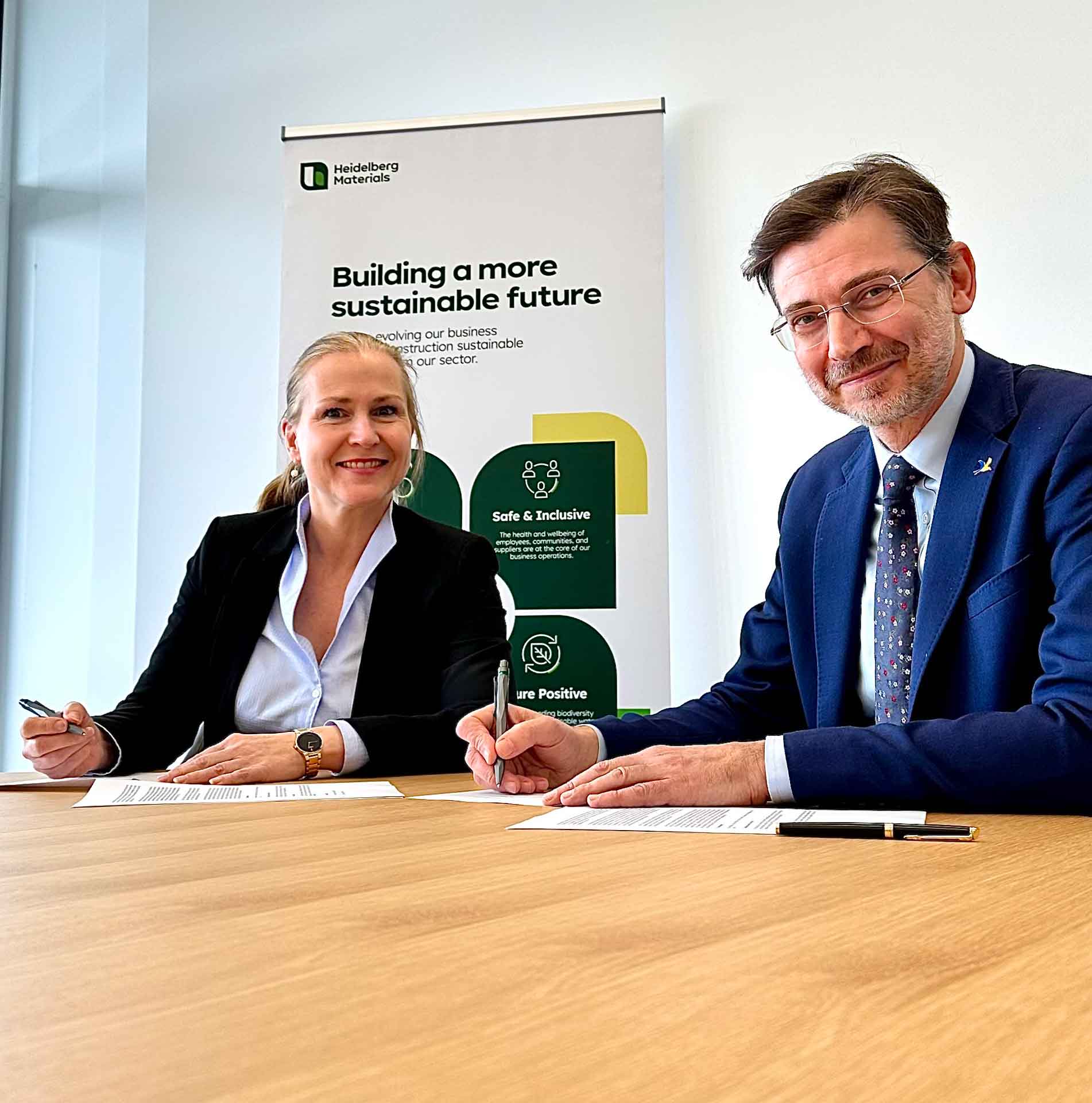 Dr Nicola Kimm and Martin Harper sitting on a table signing a memorandum of understanding