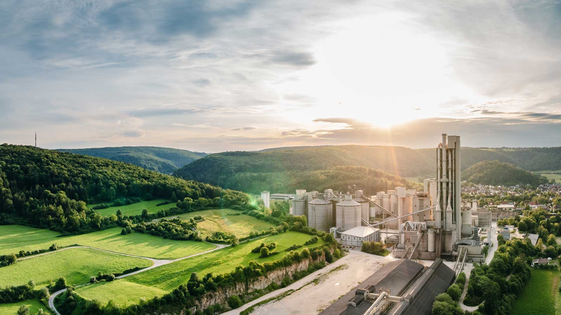 Cement plant in a green landscape, on the horizon the sun is rising