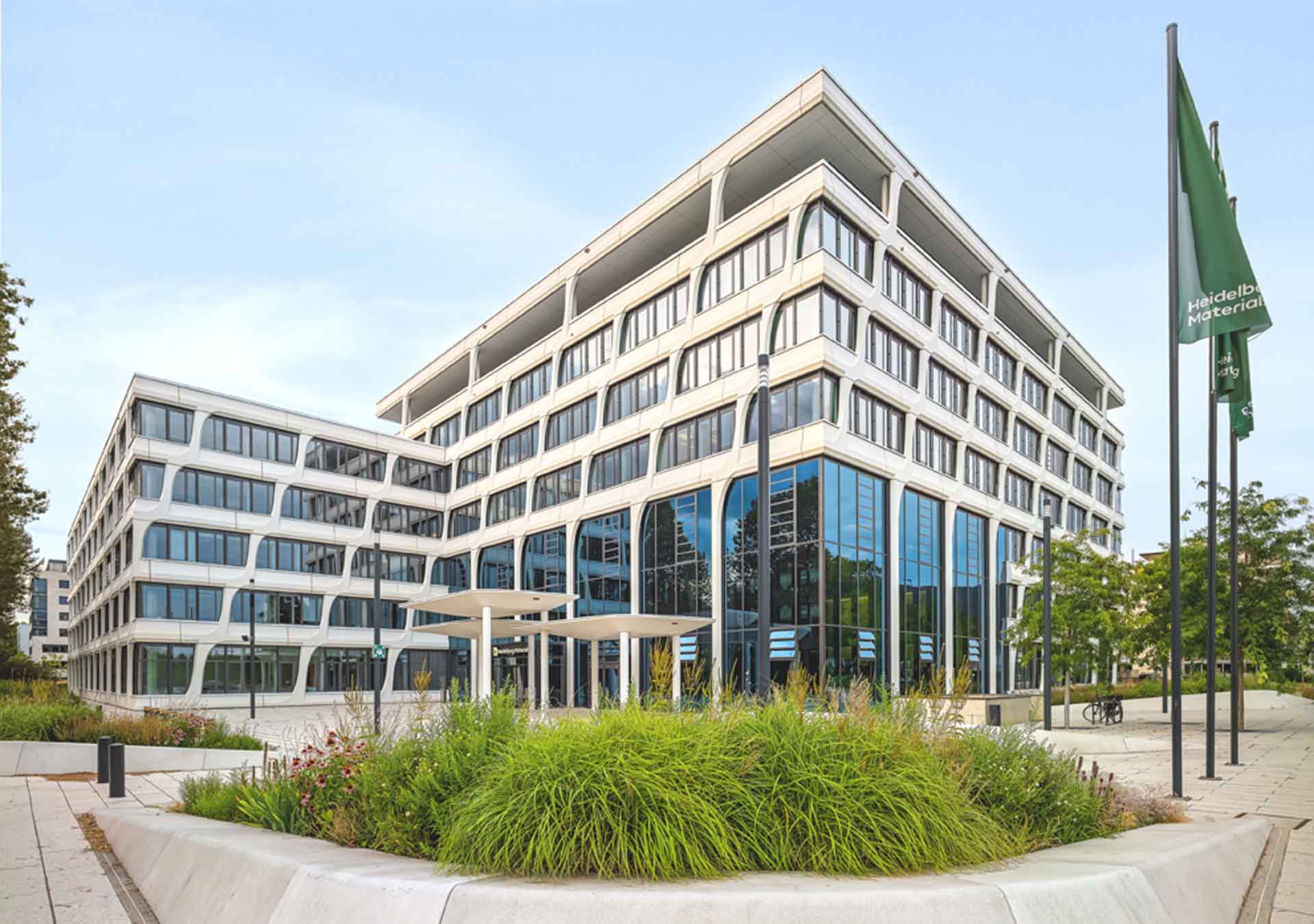 White office building, greenery in front, three flagpoles with green flags next to it