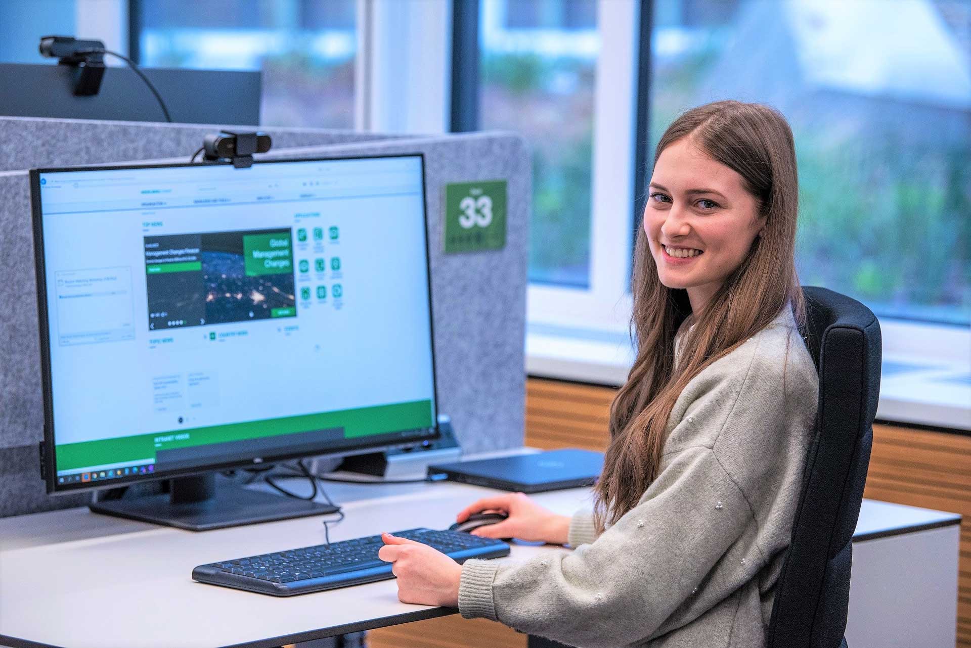 Junge Frau in einem Büro vor einem Computerbildschirm, im Hintergrund eine Fensterfront