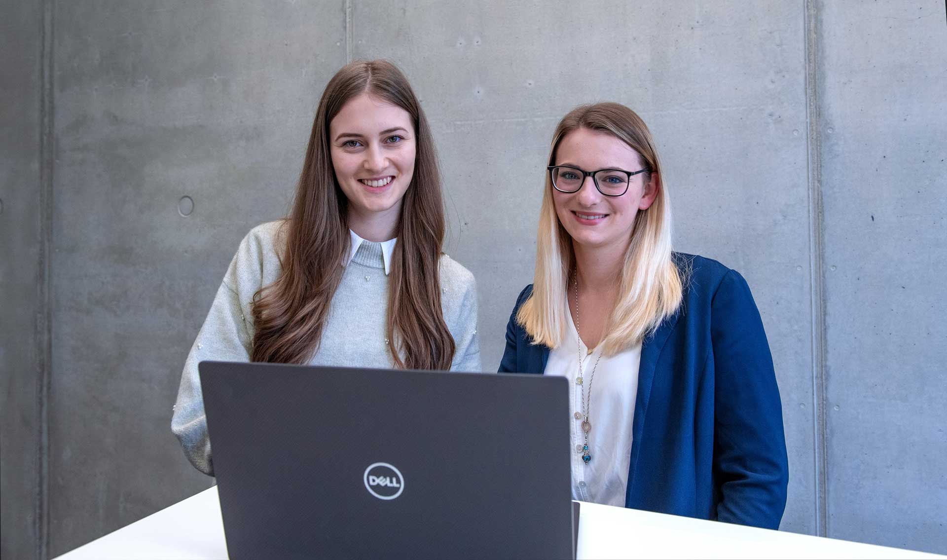 Zwei Frauen an einem Stehtisch schauen zusammen in einen Laptop