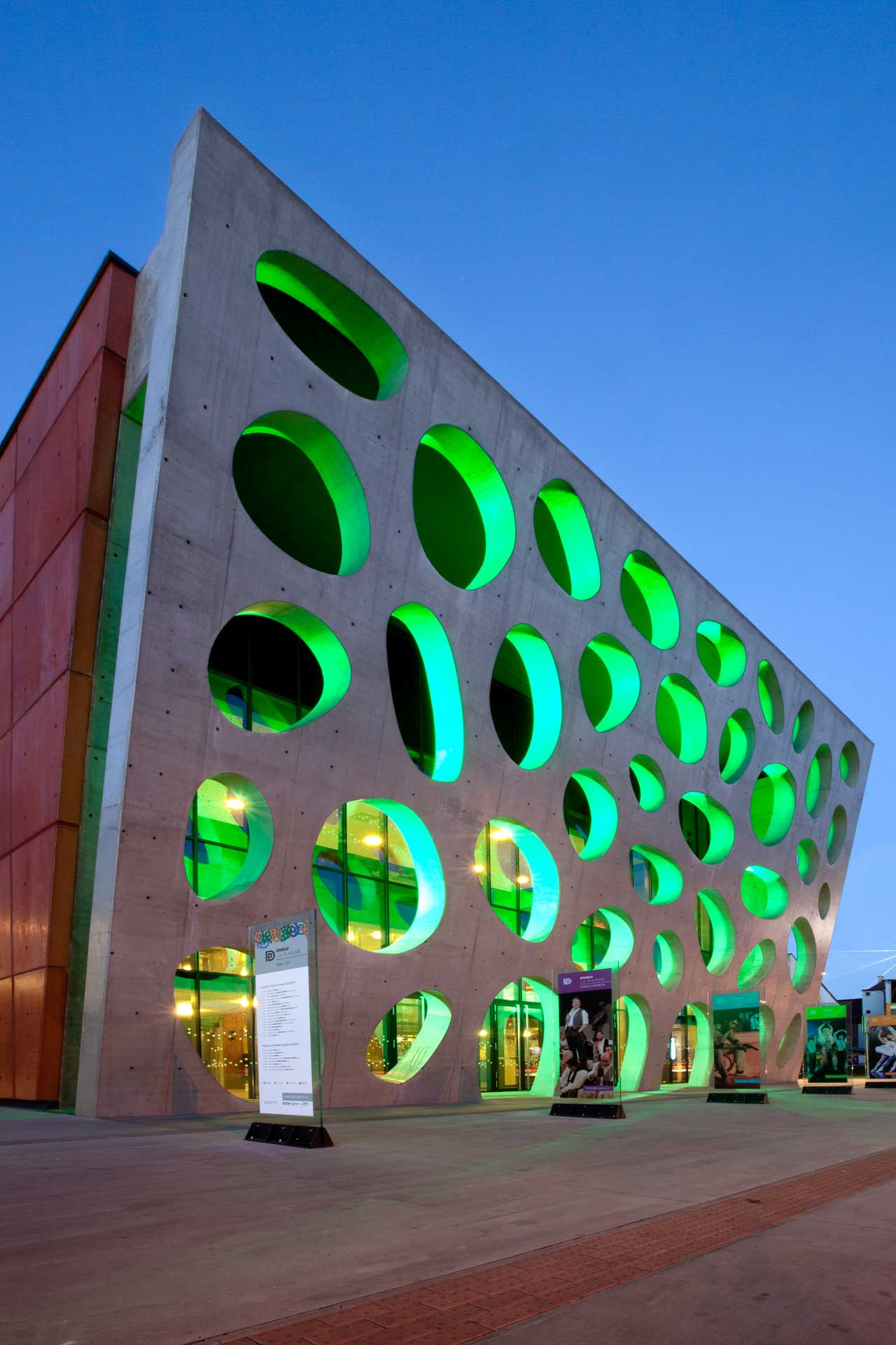 A contemporary building with a dark facade and a contrasting red-coloured facade with a perforated design.