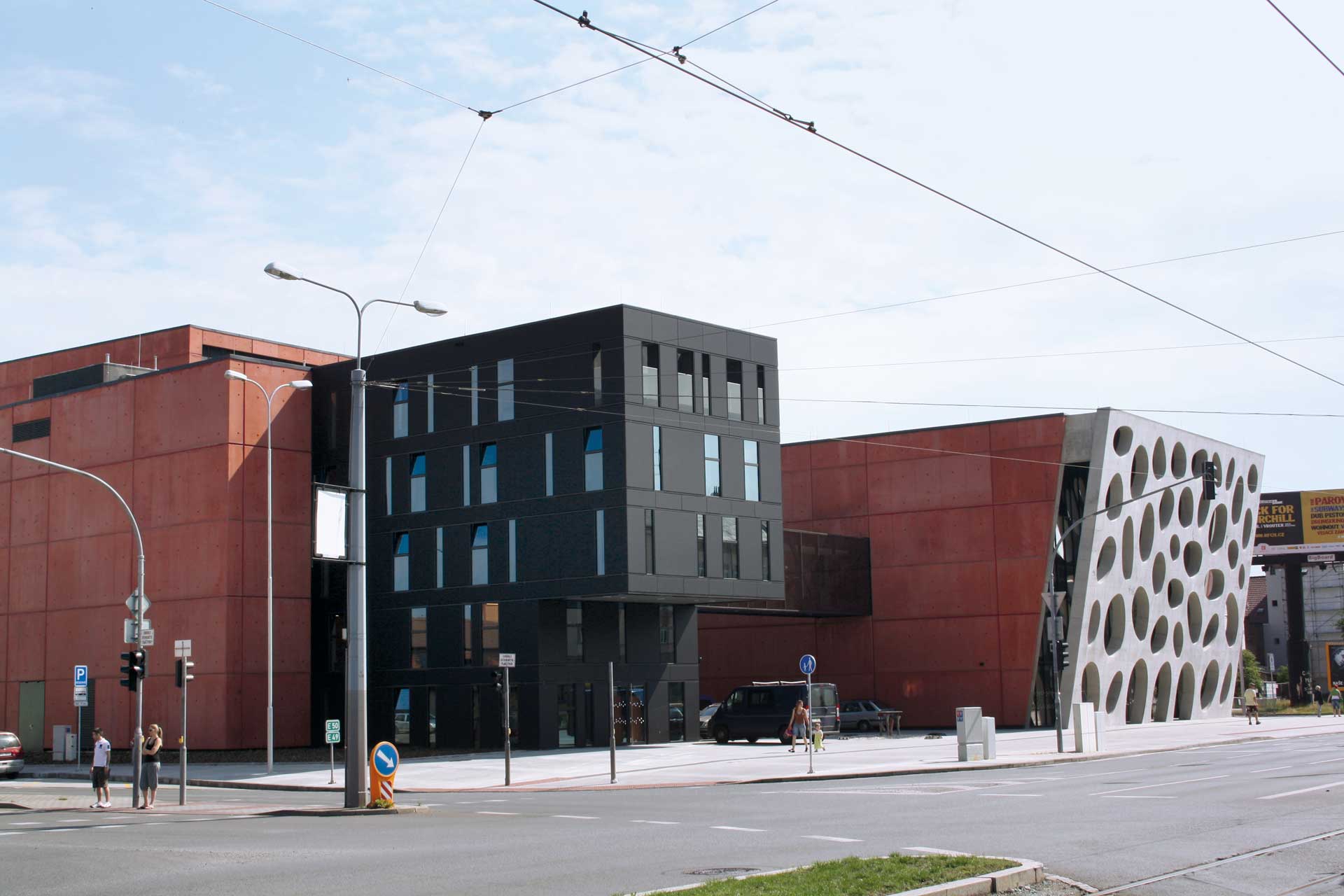 A contemporary building with a dark facade and a contrasting red-coloured facade with a perforated design.