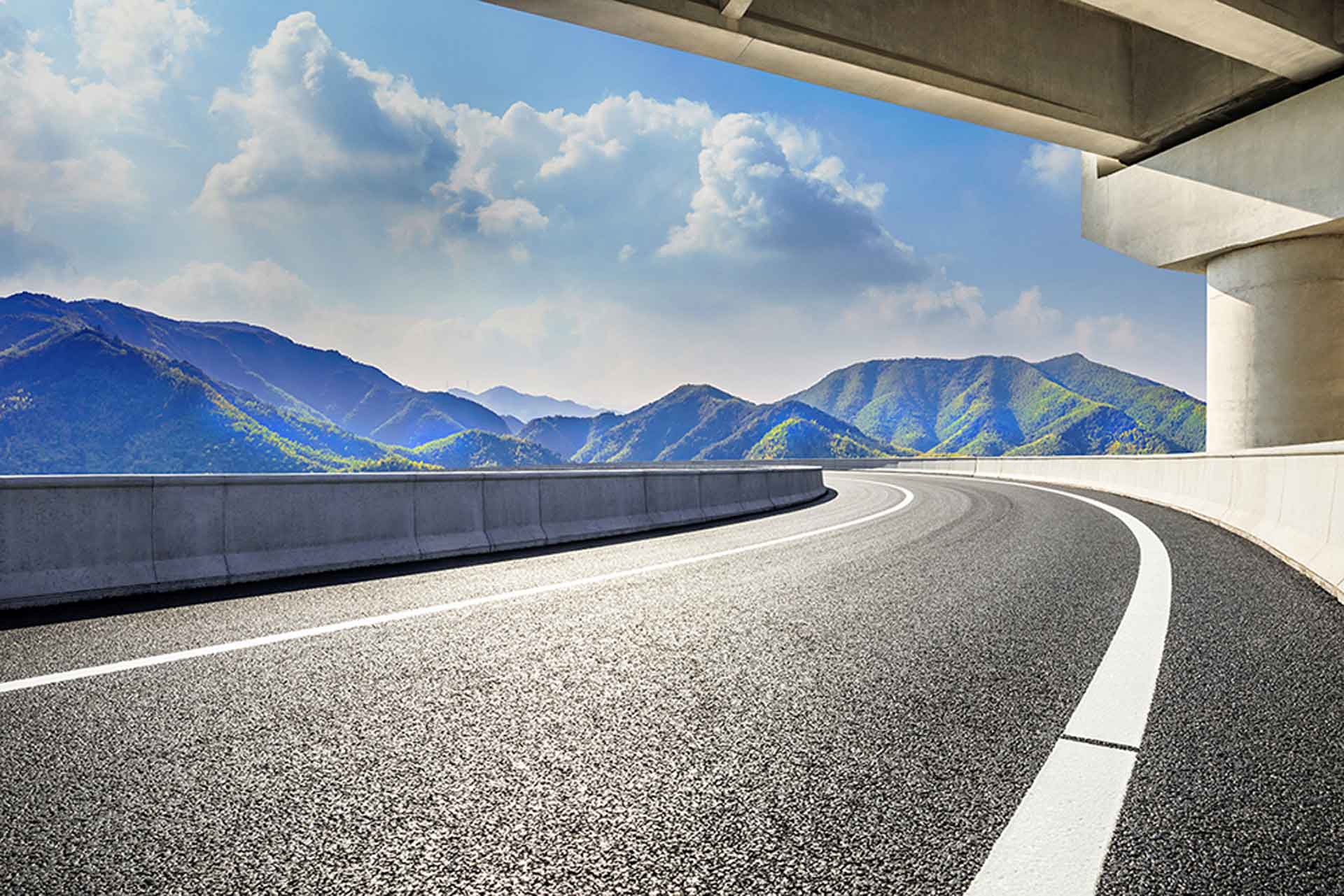 An empty road leading towards the mountains and crossed by a bridge