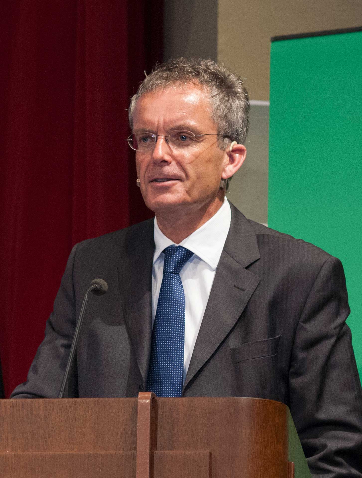 grey-haired man wearing a suit and tie at a lectern