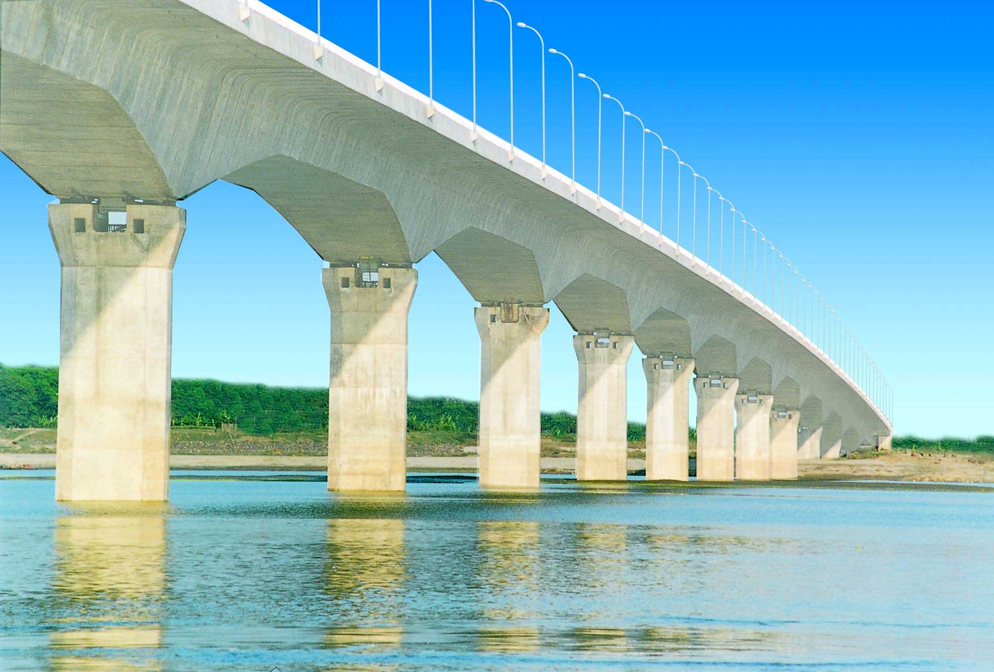 A long bridge with multiple arches spans over a river. The bridge has a series of identical, evenly spaced supports and a flat roadway on top with railings on either side.