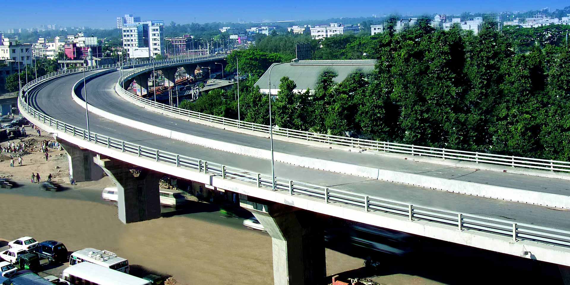 Eine erhöhte Straße, die nach links abbiegt und sich über das Bild erstreckt. Unter der Straße sind Gebäude und Bäume zu sehen, was auf eine städtische oder vorstädtische Umgebung hinweist.