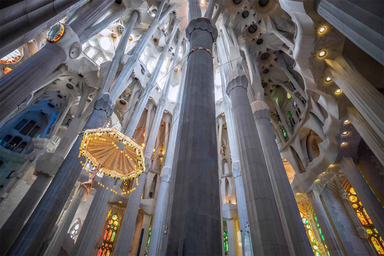 The image captures the stunning interior of Barcelona’s Sagrada Família, showcasing its iconic columns that soar towards the ceiling and the mesmerizing stained glass windows bathing the space in a kaleidoscope of colours.