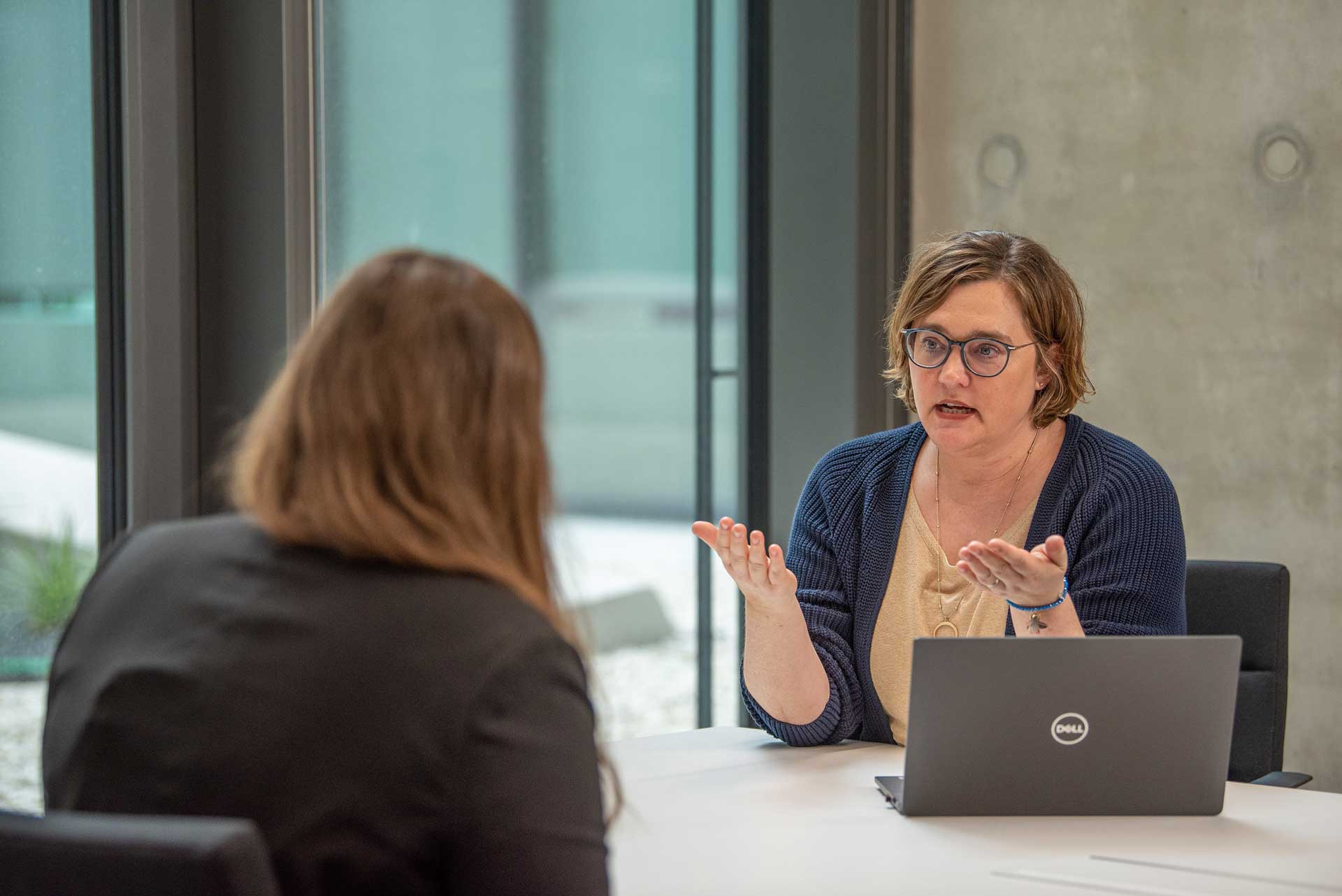 Zwei Frauen sitzen sich an einem Tisch gegenüber, auf dem ein Laptop steht