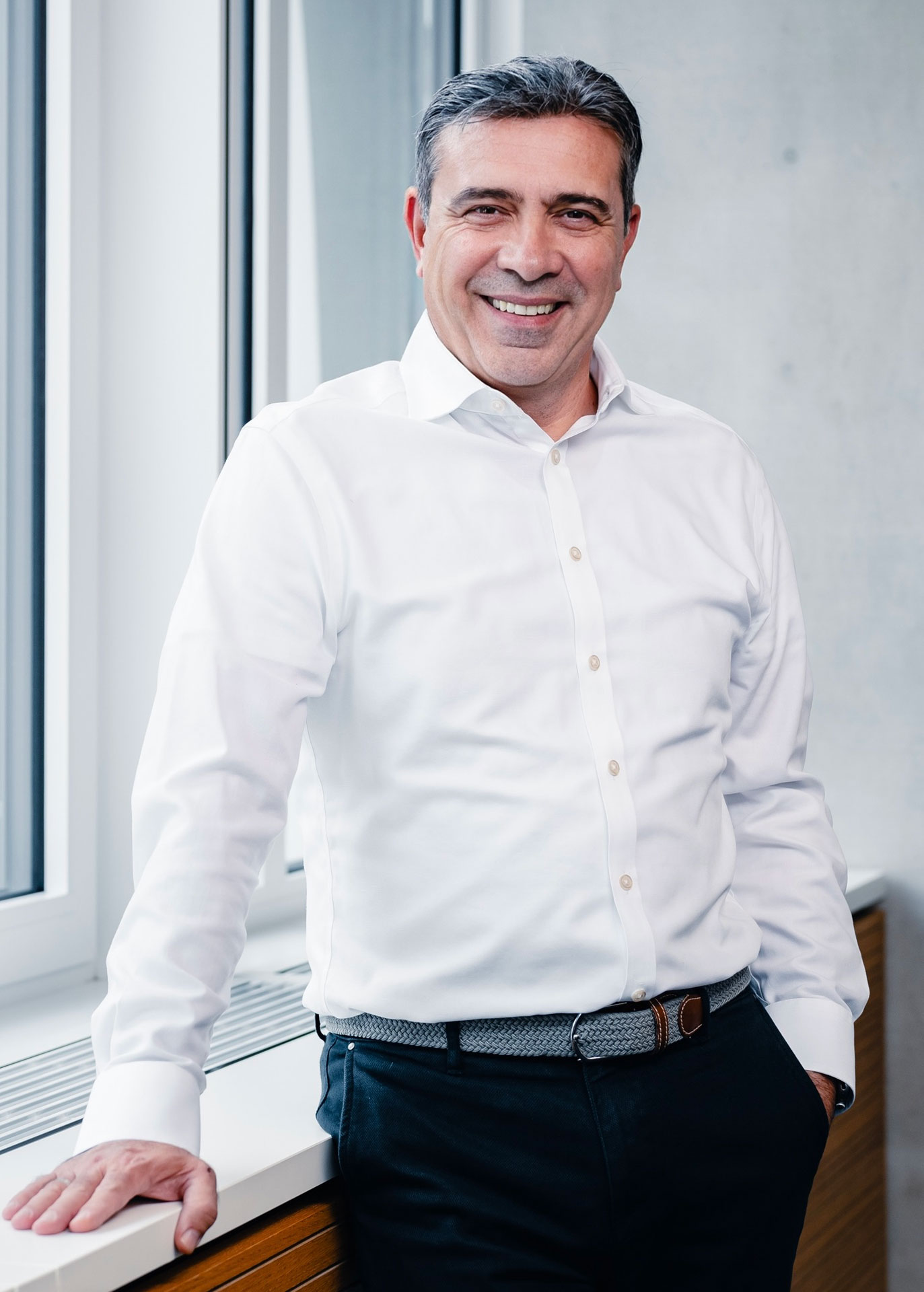 Ozan Kacar wearing a white shirt standing in front of a window, one hand on the windowsill