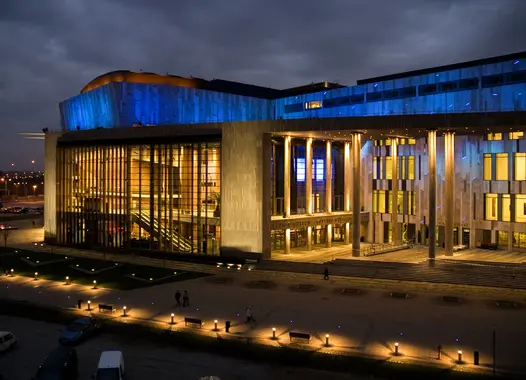 Ein zeitgenössisches Gebäude sticht in der Dämmerung hervor, sein gewölbtes Dach mit blauen Lichtern geschmückt, während warme Innenbeleuchtung sein modernes Design und die einladende Atmosphäre offenbart.