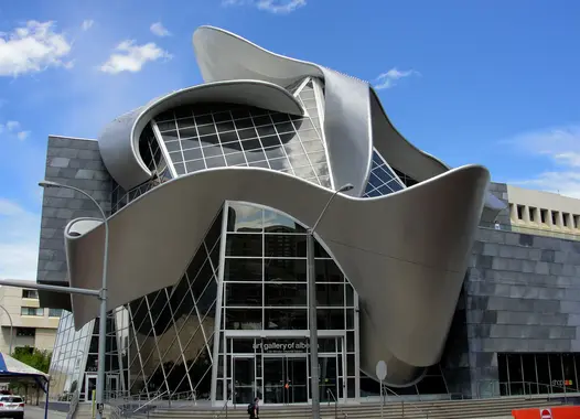 Ein modernes Kunstmuseum mit einem markanten architektonischen Design, das metallische Kurven und Glaselemente unter einem blauen Himmel mit Wolken aufweist
